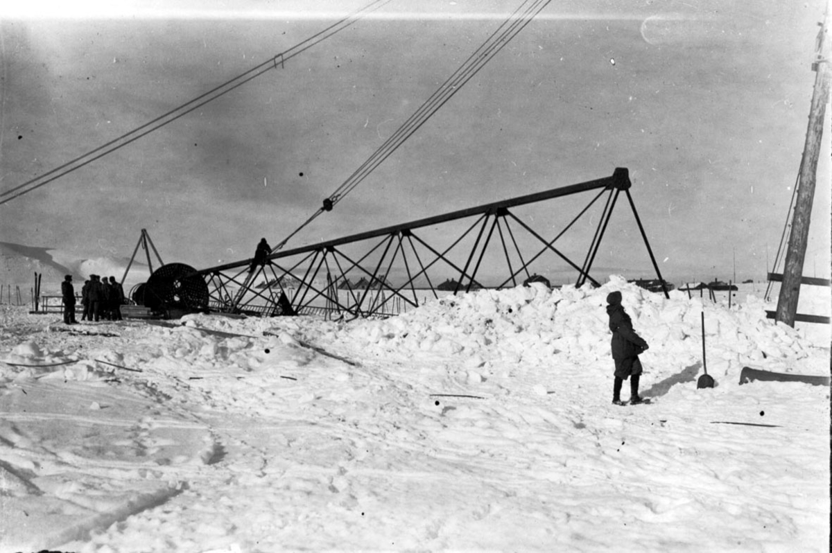 Fortøyningsmasten til luftskipet "Norge" før den heises på plass. Flere personer i arbeid. Snø på bakken.
