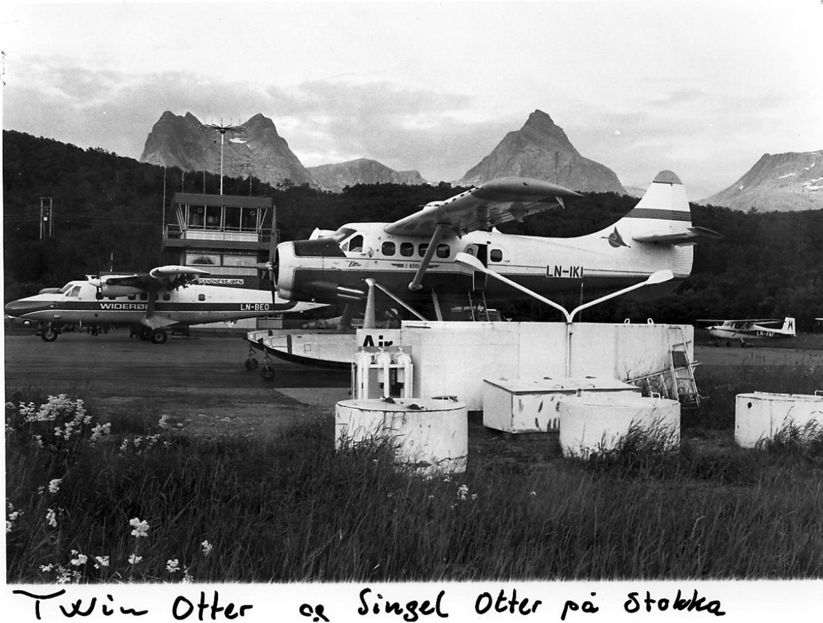 Lufthavn, 3 fly, bak t.v. DHC-6 Twin Otter, LN-BEO, fra widerøe, sett fra siden. Foran DHC-3 Otter, LN-IKI, fra Norving, sett fra siden. Mindre fly t.h. Bak sees kontrolltårnet. Fjell i bakgrunnen.