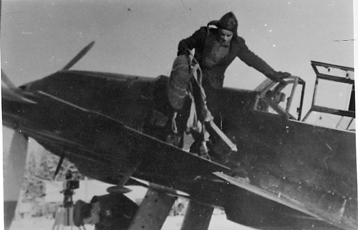 1 fly på bakken, Messerschmitt BF 109. Forparten og noe av cockpit. 1 person, pilot, på vei ut av flyet.