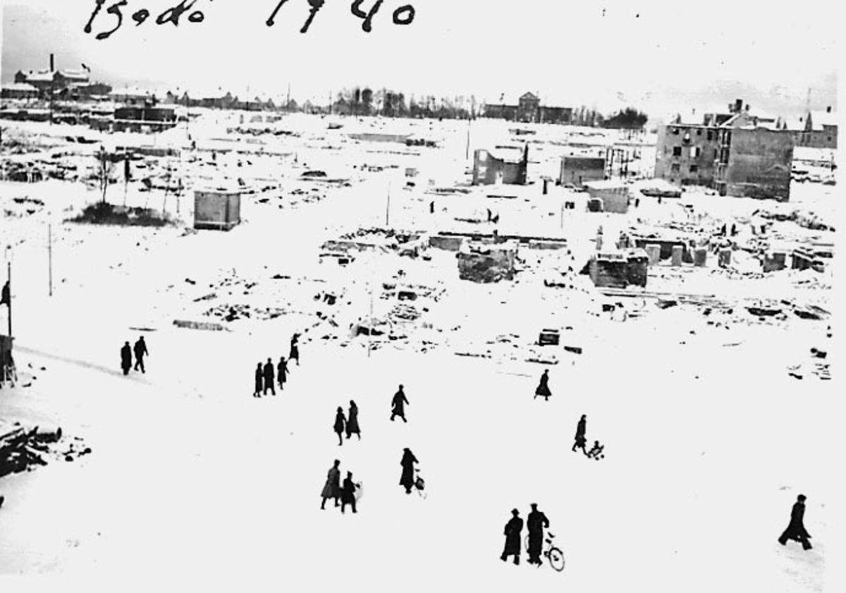 Bodø i ruiner etter bombingen under 2. verdenskrig. Snø på bakken. Flere personer blant ruinene. Fra torget, museet ses i bakgrunn.