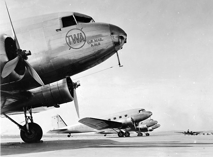 Lufthavn, flere fly på bakken. Douglas DC-2 fra TWA. Står på rekke bortover. Litt av bygninger t.h.