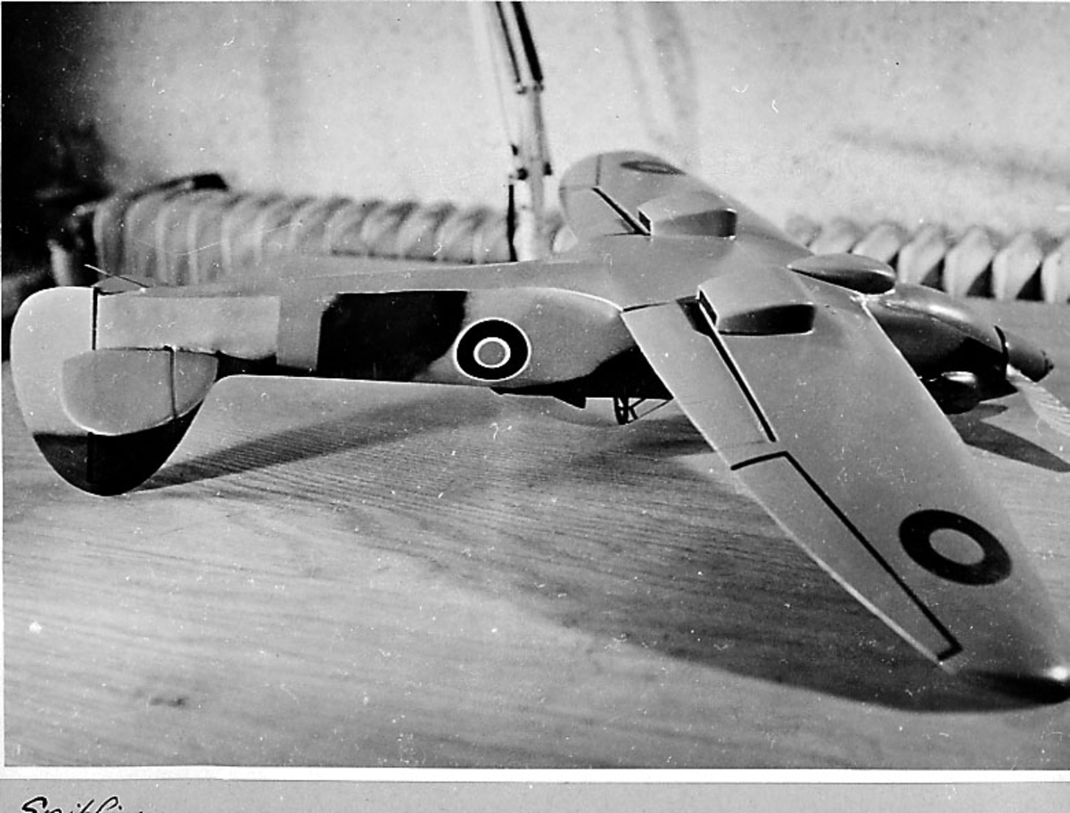Fra album. 1 foto av modellfly, spitfire IV/XII, oppstilt på en benk, på¨rygg.