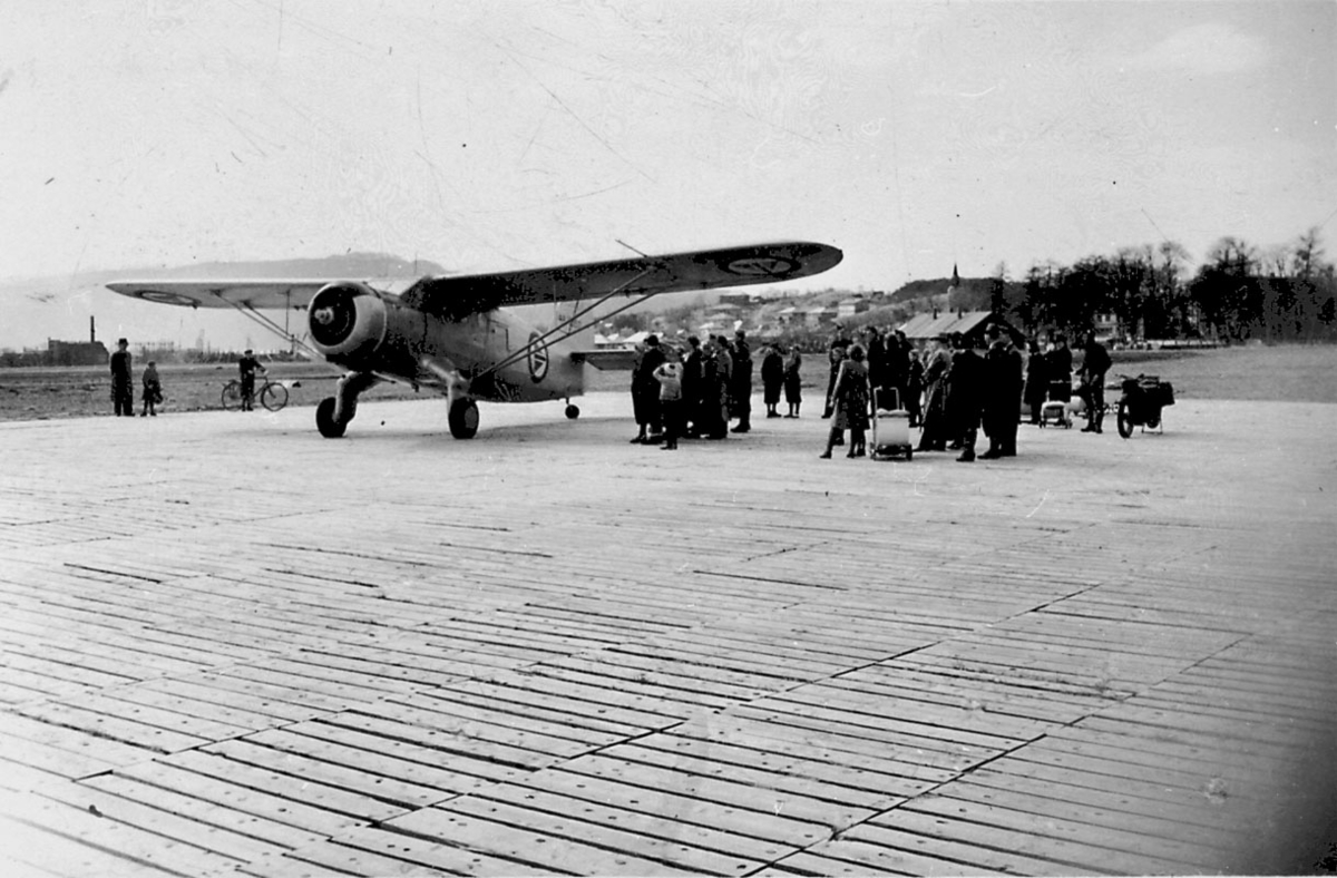 Lufthavn 1 fly på bakken, Norsemann VI, 44-70517 (R-AH) fra RNoAF, står på rullebane av plank. Mange personer ved flyet.