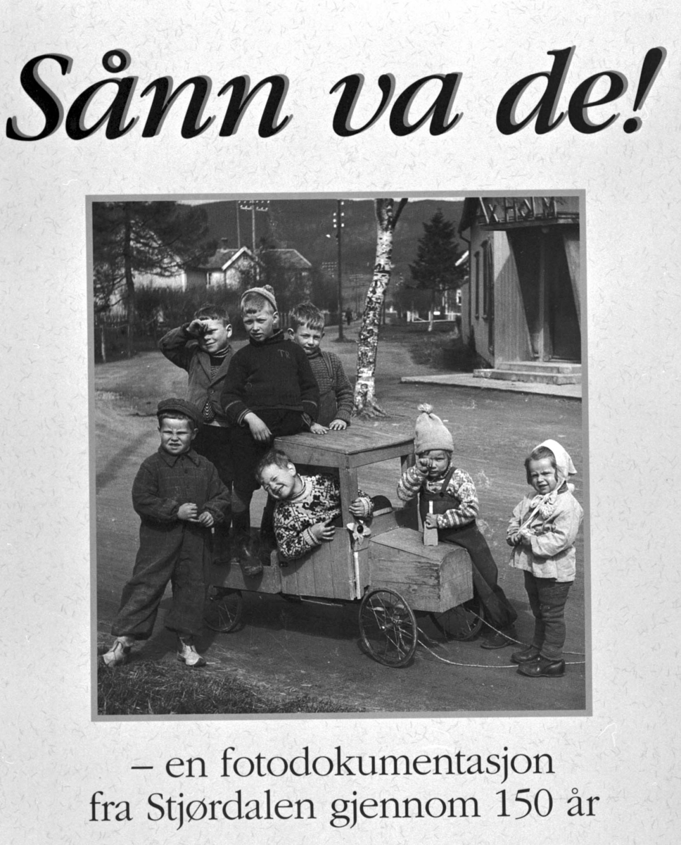 Foto fra boken "Sånn var de!". Portrett 7 personer, barn i en lekebil.