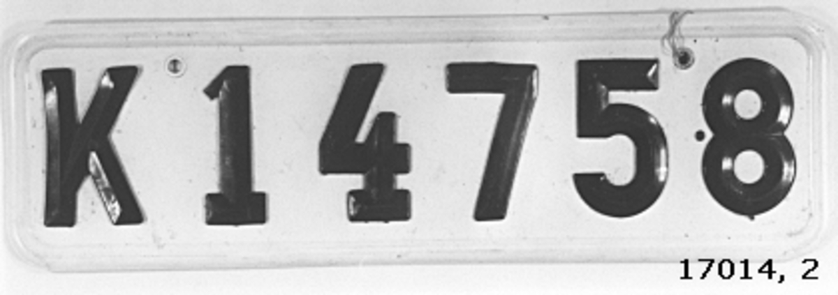 Skylt av plast, vit botten, svarta bokstäver och siffror fastnitade " K 14758 ".