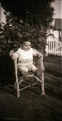 Liten gutt sitter i en stol ute i hagen på Jøraholmen, rundt