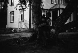 En kvinne med et barn på fanget sitter i et tre foran et hus