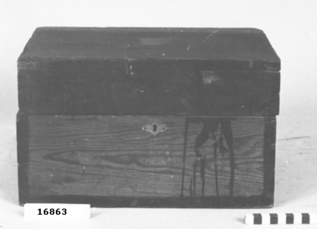 Skrin av delvis svartmålad furu med djupt lock på gångjärn. På framsidan lås med nyckelhål inom ornerat beslag av vitmetall. På lockets insida är tre delvis trasiga pappersmärken fastklistrade (47 x 47 mm) föreställande teckningar av indianer i flerfärgstryck. Med blyerts "2 - 96 Dahlberg" skrivet flera gånger på skrinets insida. På baksidan "1 - 35".