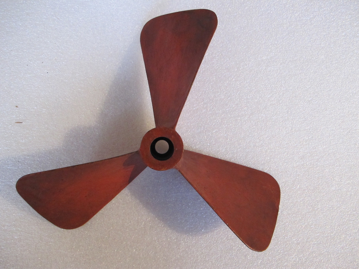 Modell av trebladig propeller i rödmålad järnplåt.