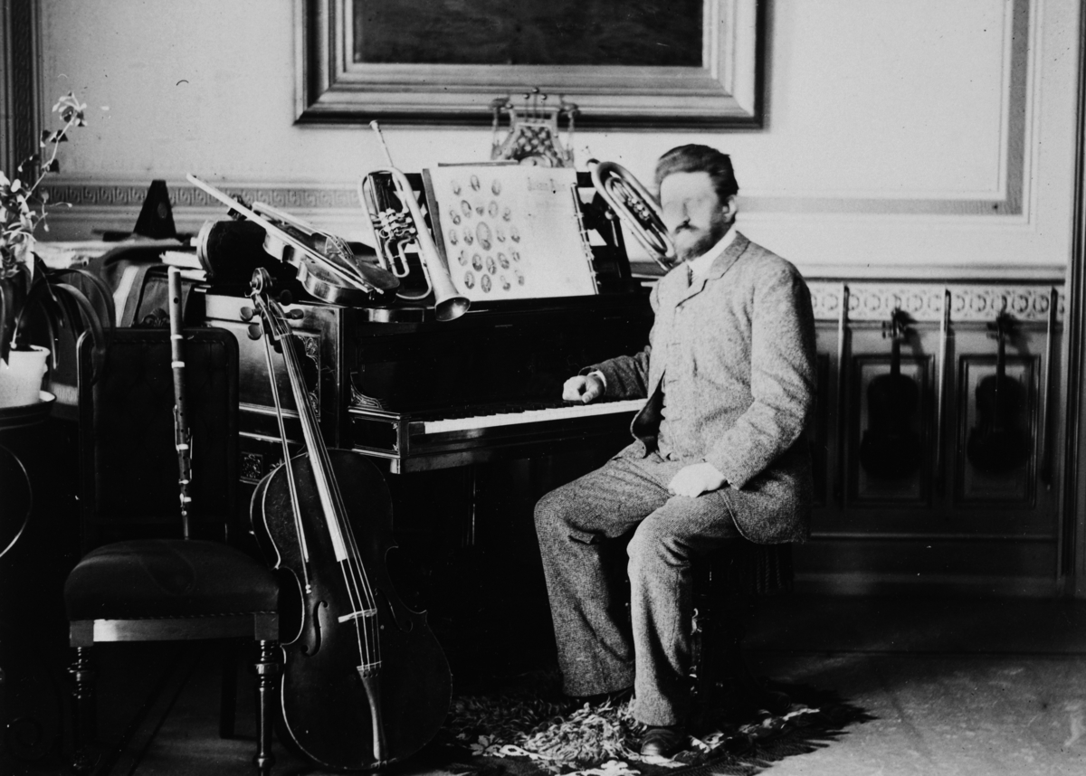 Tollef Nielsen Myklebye sittende ved et piano, omgitt av flere av hans andre instrumenter. Musikker.