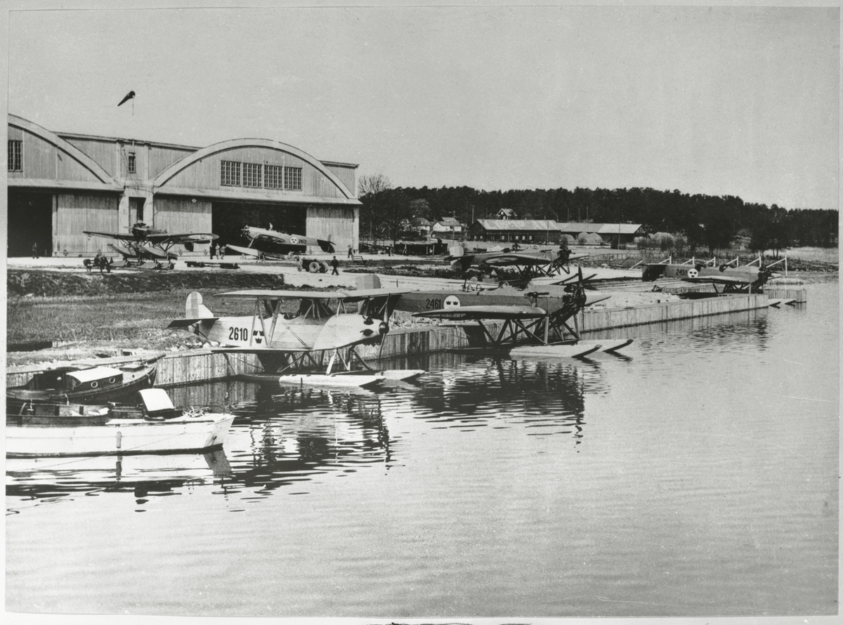 Övrigt: Från sjöflygflottiljen F2 i Hägernäs. De flesta flygplanen på bilden är av typ Heinkel HE 5/t, i Flygvapnet benämnt S 5A eller Hansa; de flygplansnummer som kan urskiljas är 2461, 2472 och 2451. De första Hansorna levererades till Flygvapnet 1927, och den sista togs ur tjänst 1945. Maskinen t v i förgrunden, övningsflygplanet Ö7 (Svenska Aero S-10 Piraten) var i tjänst 1929-37. Det bar ursprungligen nummer 210, men detta ändrades senare till 2610, som på bilden.