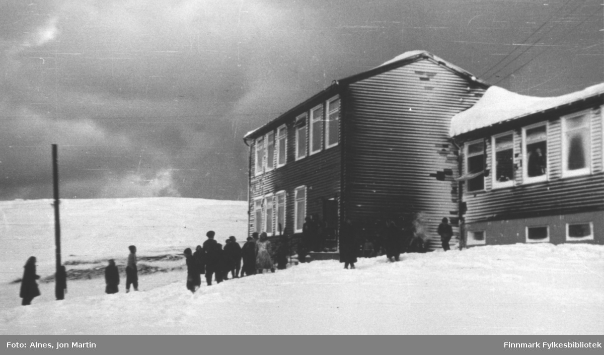 Øksfjord barneskole etter vintervær, 1954. Elevene tar oppstilling foran inngangen