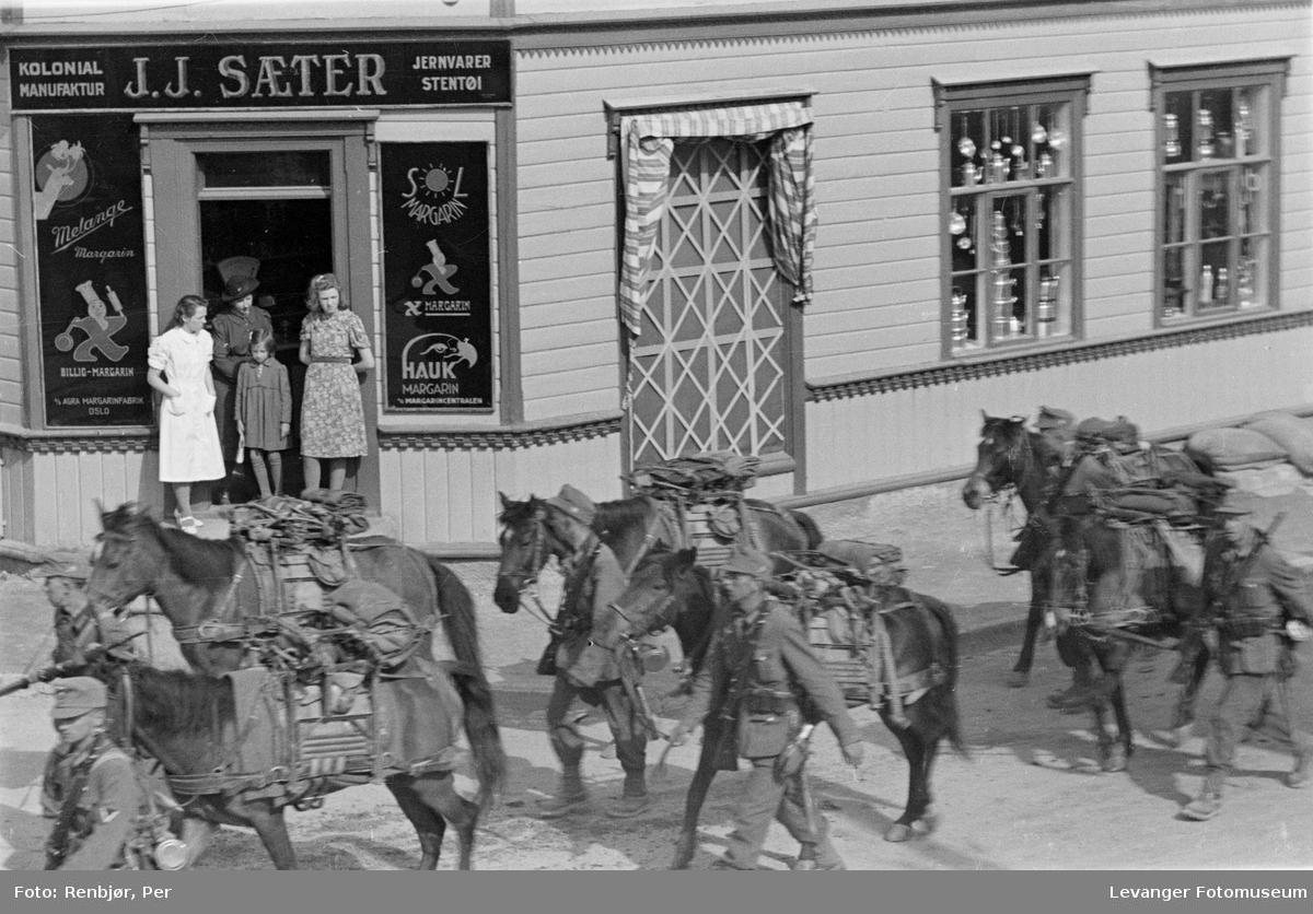 Gatescene tatt fra 2.etasje. Tyske soldater passerer med kløvhester, mens jentene observerer fra gatehjørnet.