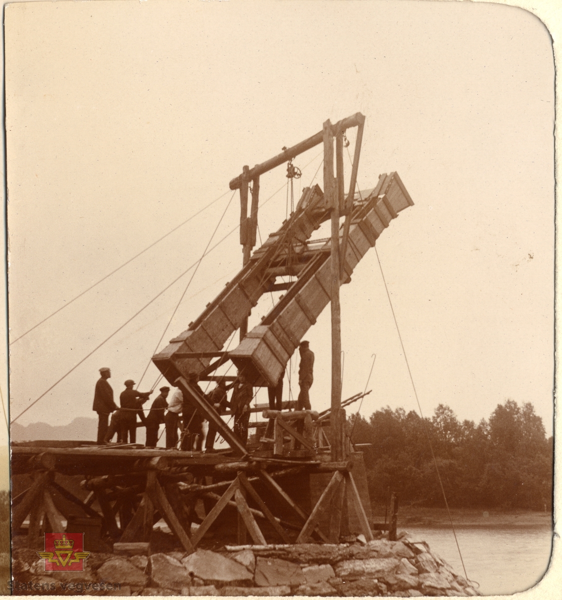 Øvre Salangen bru under bygging. Spennvidde er 54 meter. Bildet viser en gruppe menn i arbeid med brua. Heising av ferdige forskalingskasser til støping av brutårn. 1913 Øvre Salangen bro stod  på brutårnet da brua var ferdig.