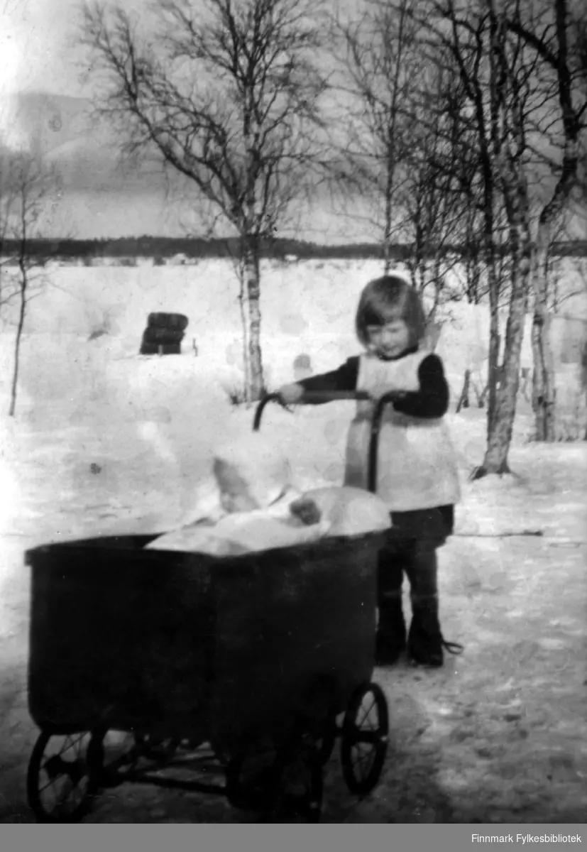 Fotografi av Mirjam Kälkäjä (f. Ranta) som står og holder i en barnevogn. I vogna sitter hennes lillebror Jarkko. Bildet er antatt å være fra ca. 1944 og er tatt på finsk side av Pasvik.