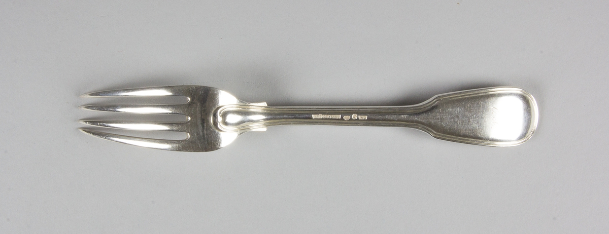 Gaffel av silver med fyra klor. På skaftets ovansida löper en kant som i övre änden avslutas i en hjärtformad spets. Med stämplar på skaftets baksida.