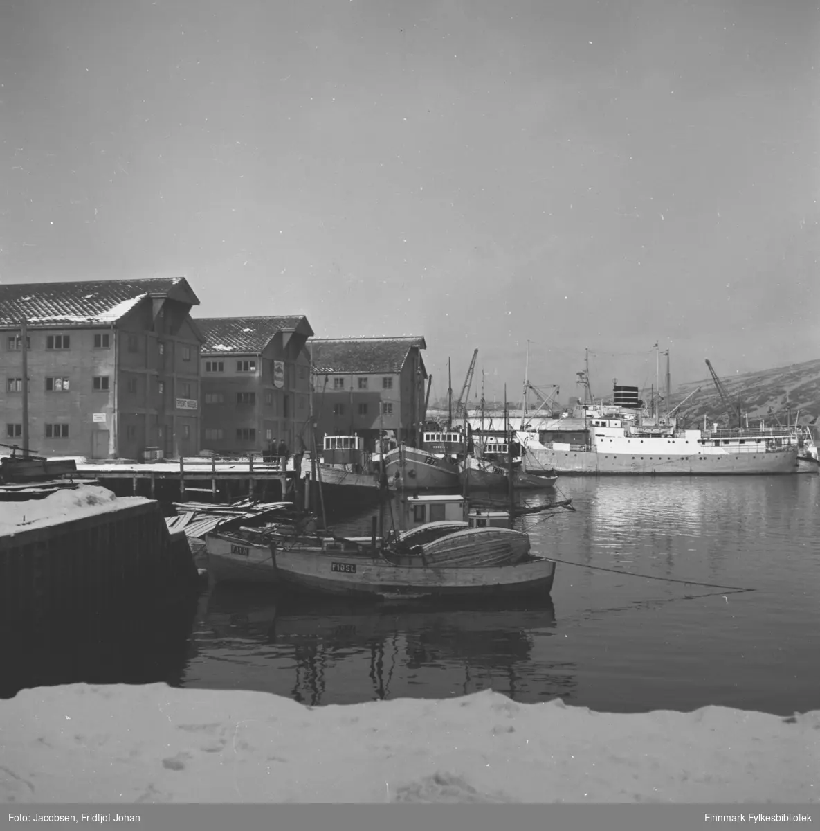 Hammerfest havn med noen fiskebåter ved kai. Den store båten til høyre i bildet er en FFR-båt, MS Brynilen (den har navnet etter et sted i Loppa kommune, nær grensa til Kvænangen). Bak Brynilen ligger den bergenske 15-mileren MS Ara. De store byggene på kaia er Trygve Nissens forretning og lager. Lengst borte ligger Televerkets lager som i dag huser biblioteket.