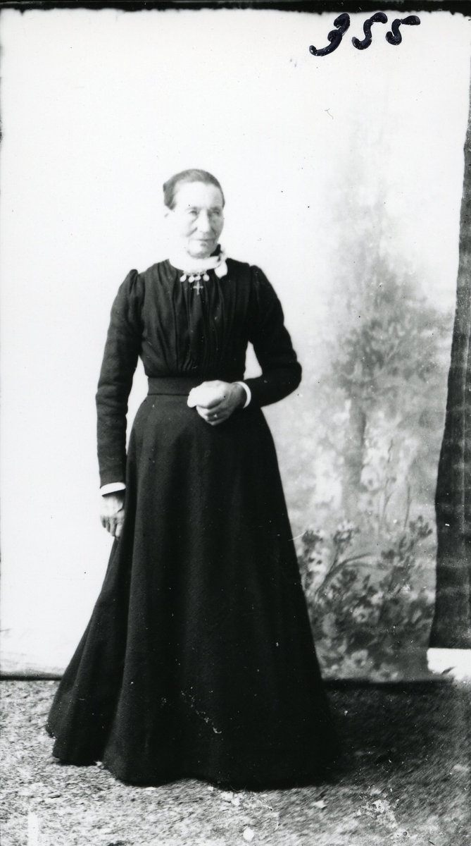 Portrett i helfigur av Marit Ferden, født Røn. Avbildet foran lerret i lang, svart kjole.