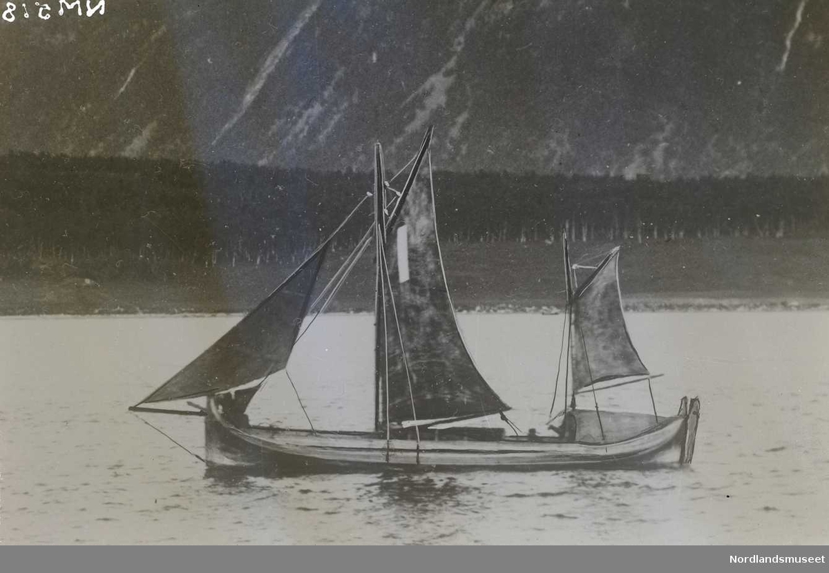 Nordlandsbåt, åttring med sneseil, på vei ut fjorden. Fjell i bakgrunnen. Snø i fjellene.