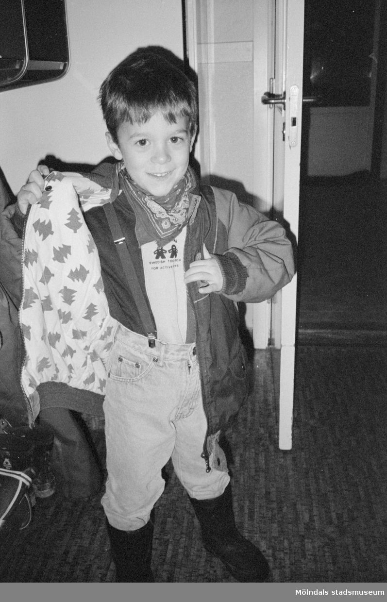 En pojke öppnar sin jacka och visar fordret på insidan som är tryckt med granar på ljus botten. Han står i entrén till Katrinebergs daghem, 1992.