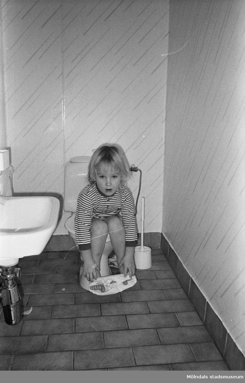 Ett barn som sitter på toaletten. På golvet ligger klinkers och till vänster syns ett handfat. Lille Skutt, Katrinebergs daghem, 1992.