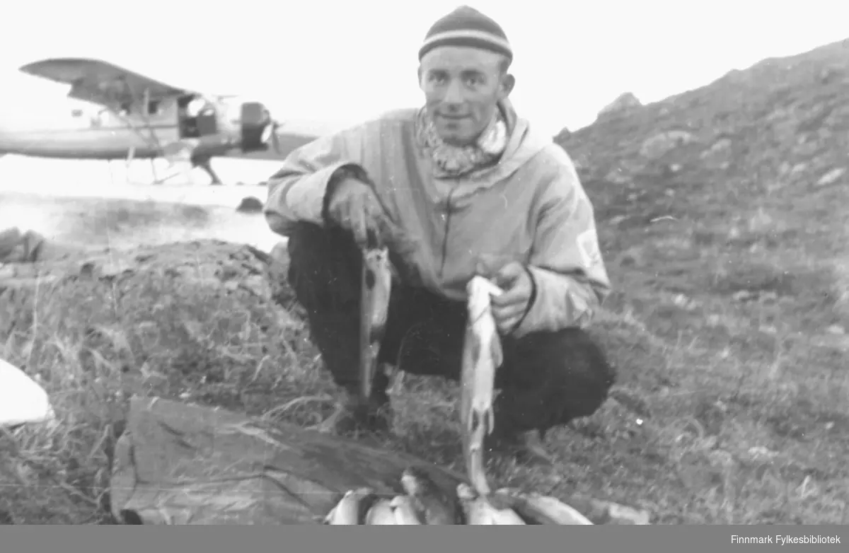 Dette bildet er tatt i løpet av helgen 12.-13. august 1955 og del av en serie bilder tatt på  fiskertur med sjøfly til det avsidesliggende Peskvannet. Her viser Ernst Lebesby fram noe av fangsten. Foto: Per Bjørgan.