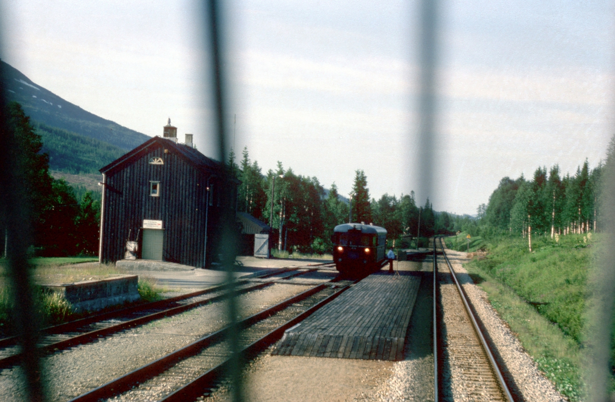 Togekspeditøren i Svenningdal viser signal "Passer" (grønt flagg) til lokomotivføreren i godstog 5794. Toget krysser med tog 475 "Majavassvogna", Majavatn - Mo i Rana.