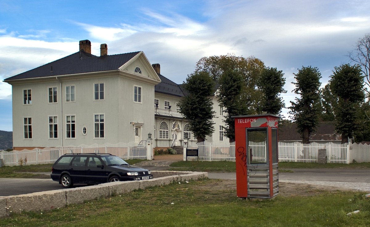 Denne telefonkiosken står ved Austad herredshus, Styrmoes vei 33, Drammen. Den er en av de 100 vernede telefokioskene rundt om i Norge. De røde telefonkioskene ble laget av hovedverkstedet til Telenor (Telegrafverket, Televerket)
Målene er så å si uforandret. 
Vi har dessverre ikke hatt kapasitet til å gjøre grundige mål av hver enkelt kiosk som er vernet. 
Blant annet er vekten og høyden på døra endret fra tegningene til hovedverkstedet fra 1933.
Målene fra 1933 var:
Høyde 2500 mm + sokkel på ca 70 mm
Grunnflate 1000x1000 mm.
Vekt 850 kg.
Mange av oss har minner knyttet til den lille røde bygningen. Historien om telefonkiosken er på mange måter historien om oss.  Derfor ble 100 av de røde telefonkioskene rundt om i landet vernet i 1997. Dette er en av dem.