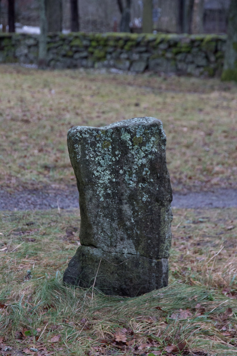 Gravsten, stående något oregelbunden rektangulär form, huggen av sten. Saknar inskription.