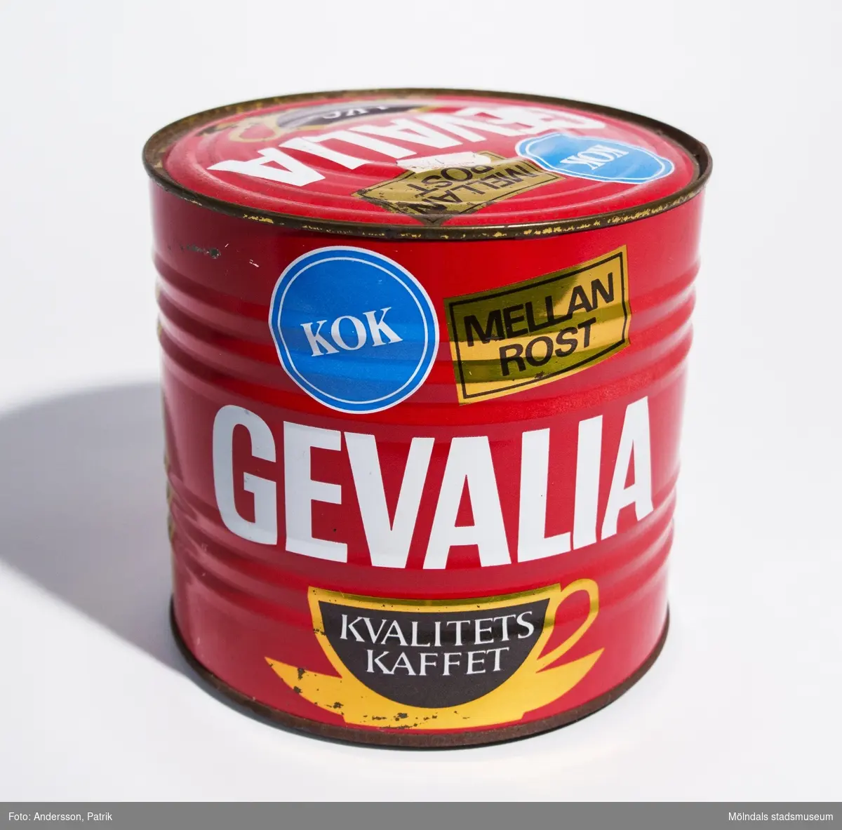 Plåtburk som innehåller 1 kg Gevalia Kokkaffe Mellanrost, tillverkat av Victor Th Engwall & Co KB, Gevaliarosteriet i Gävle. Troligtvis tillverkad mellan 1957-1971.
Burken är oöppnad. Man måste använda konservöppnare för att öppna den.

Burken är röd. På burken finns texten: "KOK MELLAN ROST GEVALIA", tryckt i färgerna blått, vitt, guld och brunt. Bredvid finns en guld och brunfärgad kaffekopp med texten "KVALITETS KAFFET". Mot guldfärgad bakgrund finns även texten: 
"KUNGL. HOVLEVERANTÖR
1 kg
Gevalias jämna och höga kvalitet uppnås genom bladning av de bästa kaffesorterna från högbelägna plantager huvudsakligen i Centralamerika, Colombia, Brasilien, Kenya och Tanzania.
Olika råkaffen varierar i kvalitet mellan olika skördar och säsonger. För att Gelvaliasmaken ändå skall vara densamma år efter år sker en ständig finjustering av blandningen, samt provning och kontroll av råkaffe och färdig produkt. 
I oöppnad förpackning bibehålles Gevalias fylliga arom under minst ett år. Sedan burken öppnats bör den förses med tättslutande lock och lagras torrt och gärna svalt.
Om Du har några frågor om kaffe eller om Gevalia - ring till oss på Gevalia Konsumentkontakt 026/10 06 80.
Gevaliarosteriet. Vict. Th. Engwall & Co, KB, Gävle"
På locket finns också en vit prisetikett (klisteretikett): "HEMKÖP CENTRALEN 17.25".
Burken är något sliten och kantstött.