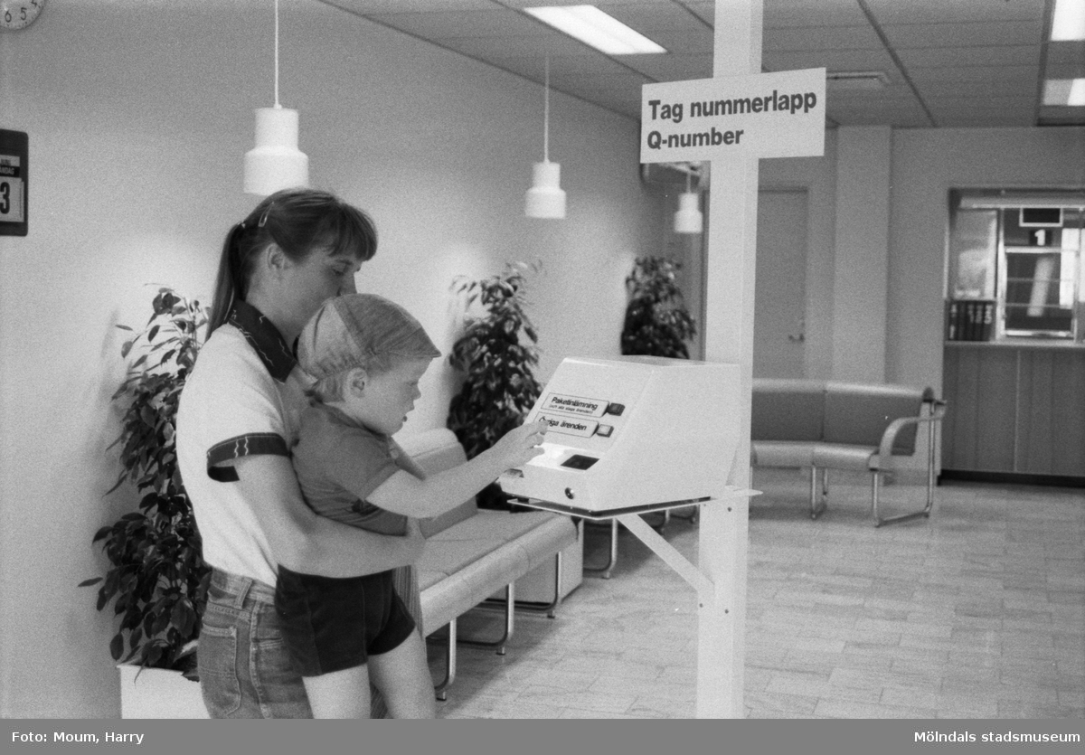 Nyrenoverade postkontoret på Jungfruplatsen i Mölndal, år 1985. "Joel Ringberg, 3 år får hjälp av mamma Majvor med att testa det elektroniska kösystemet."

För mer information om bilden se under tilläggsinformation.