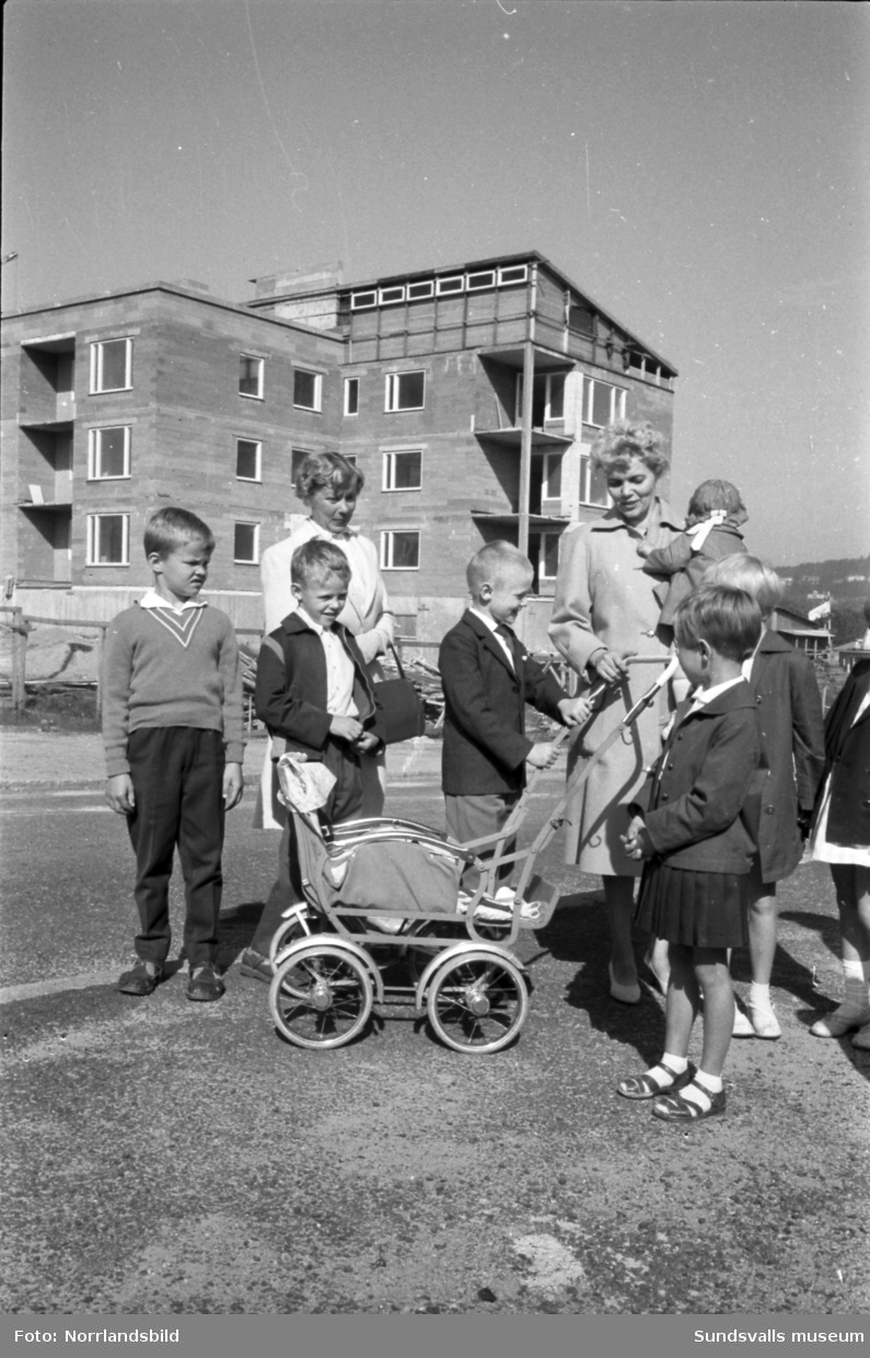 Skolstart på Sankt Olofsskolan. Förväntansfulla barn och mammor samlas utanför skolan. I bakgrunden syns kvarteret Tegen där bygget av det så kallade Långholmen pågår.