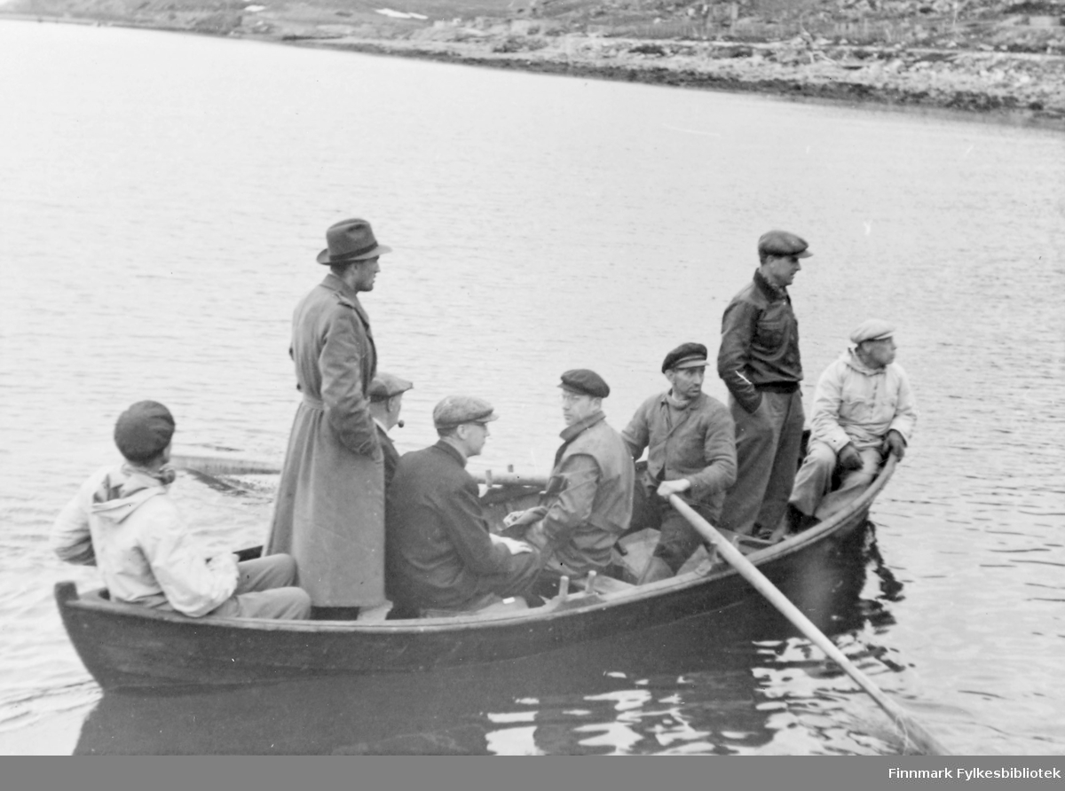 En gruppe menn ombord i en liten robåt. Alle har sixpence eller hatt på hodet.