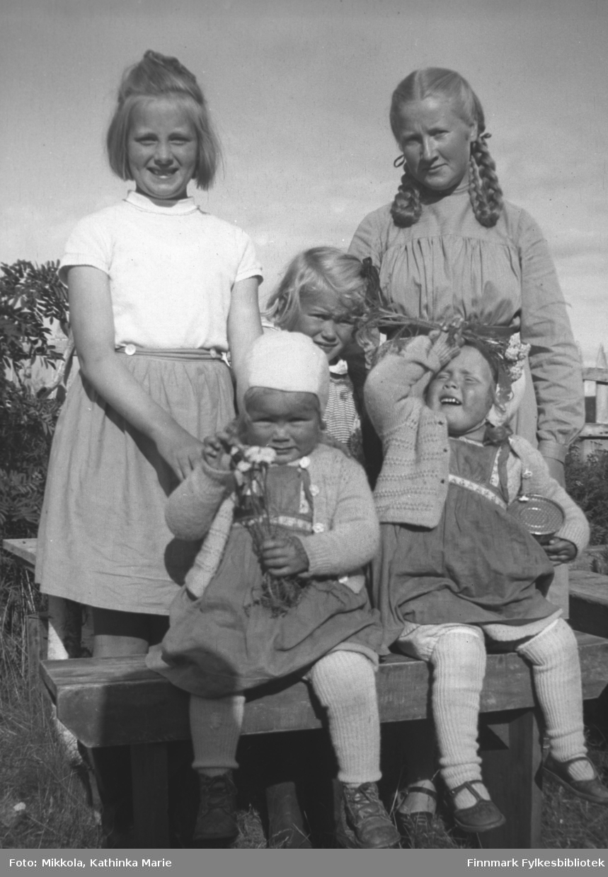 Gruppebilde en sommerdag i hagen på Mikkelsnes. Fra venstre Randi Aarvik (Vardø) og Herlaug Mikkola. I midten av bildet: Anne Marie Onarheim og foran hennes tvillingsøstre Gunvor og Torhild Onarheim. Bildet er tatt ved samme anledning som 05007-507. 