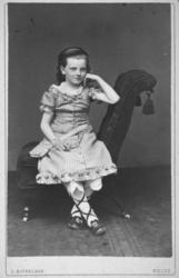 Portrett av en ung jente som sitter i en stol. Hun har en st