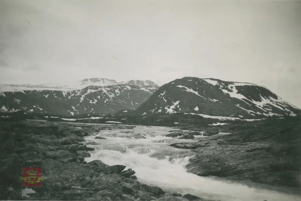Album fra 1929-1943.  Bilde fra Sjodalen/Valdresflye.  Vi ser elva Sjoa, like etter at den har rent ut av Gjende. Bildet er trolig tatt i nærheten av Maurvangbrua. Fjellene i bakgrunnen er fra nærmest: Gjendehøe, Knutshøe og Høgdebråtet, sett mot vest.
