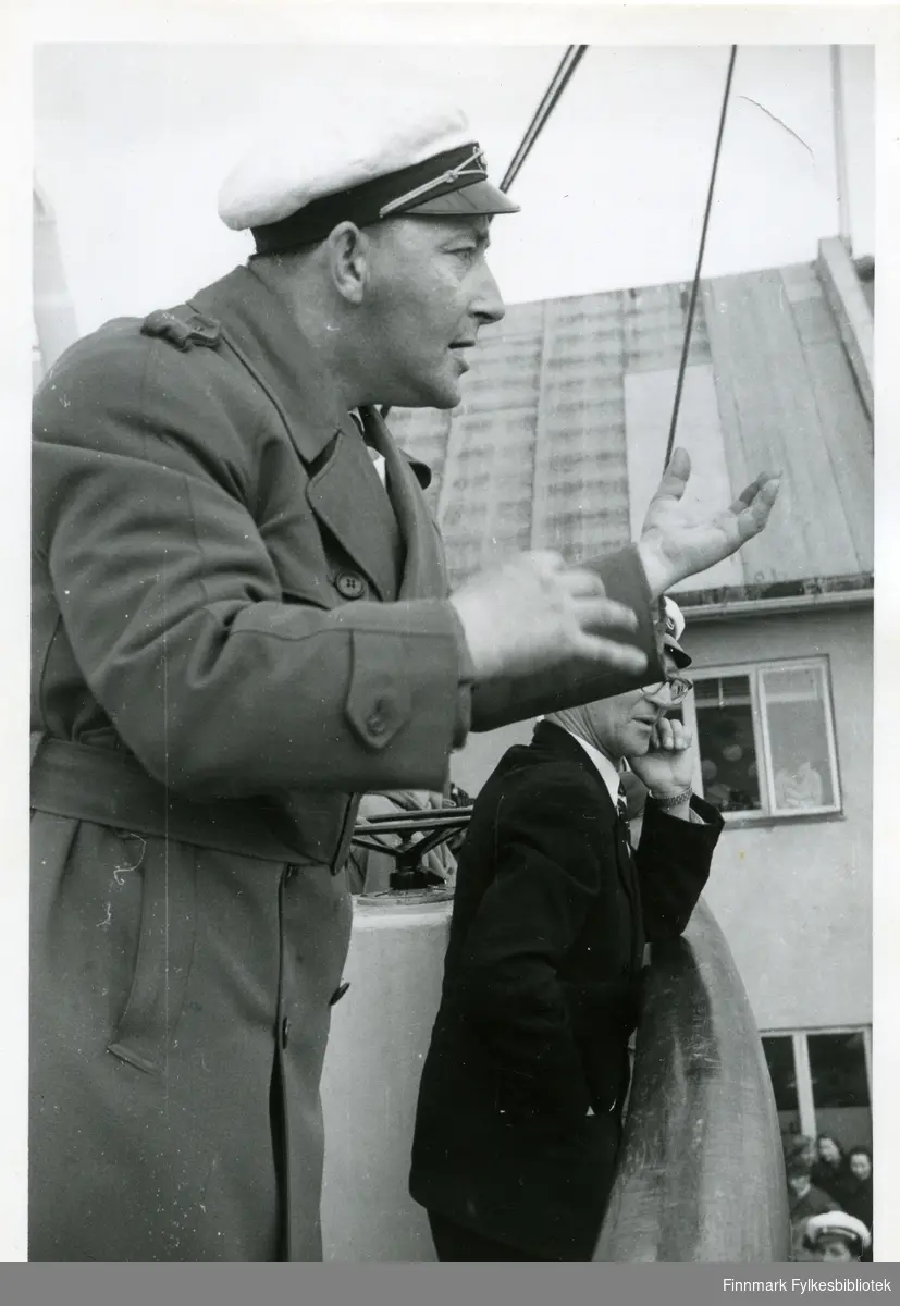 Bildet viser Rolf Olsen under korstevnet i Honningsvåg pinsen 1956. Han dirigerer et kor. På seg har han en lang jakke og hatt.  Bak ham kan man se en mann med briller lene seg mot relingen. Bak dem kan man se et hus med vindu, i vunduet kan man se tilskuere.