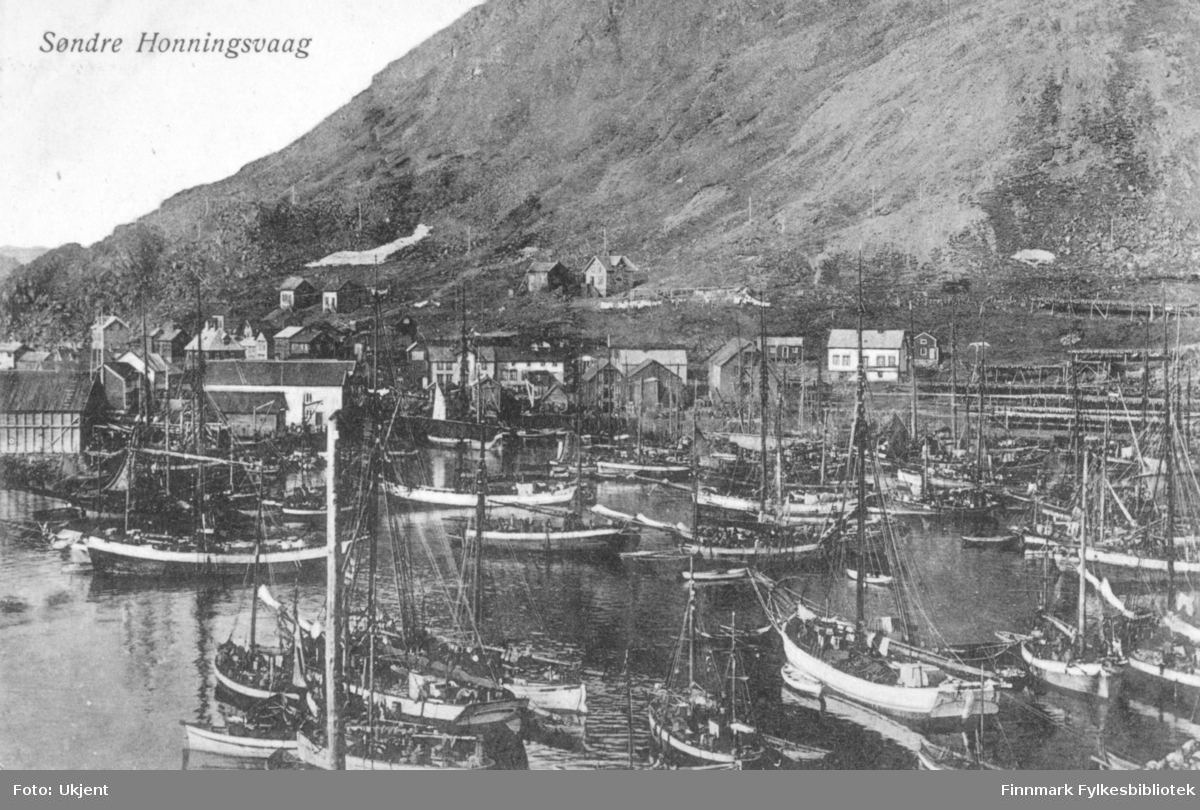 Søndre Honninsvaag som motiv på dette postkortet. På bilde kan man se en havn med flere båter til kais. I bakgrunnen ser man bygninger og fjell.