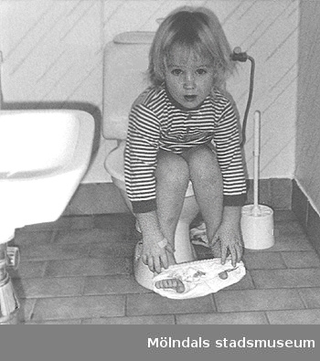 Ett barn sitter på toaletten i väntan på hjälp. Bild tagen till Mölndals museums utställning 1993 om och av daghemmet.