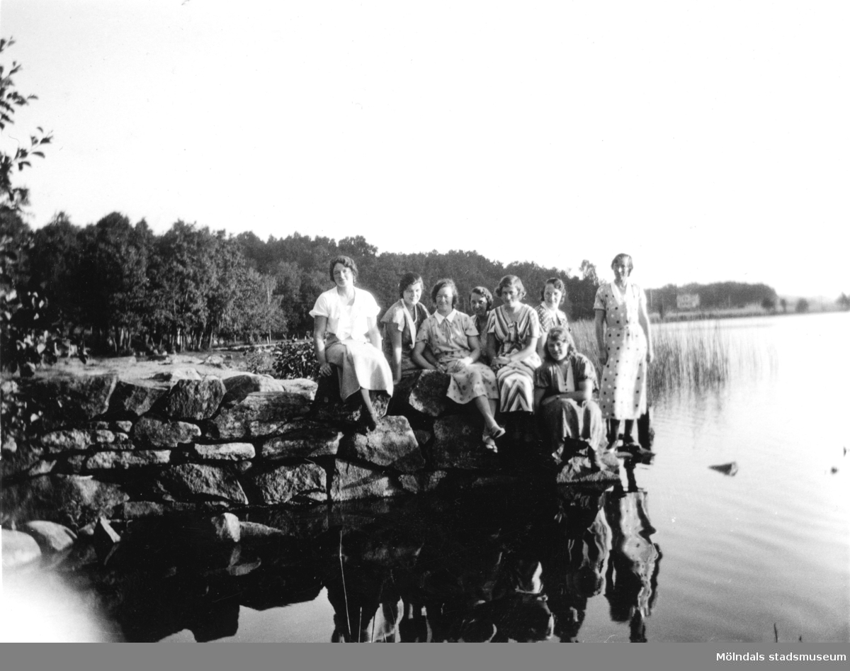 Personal från Stretereds skolhem sitter eller står på stenar vid Tulebosjön, okänt årtal. Huset i bakgrunden till höger tillhörde Gjörloffs.