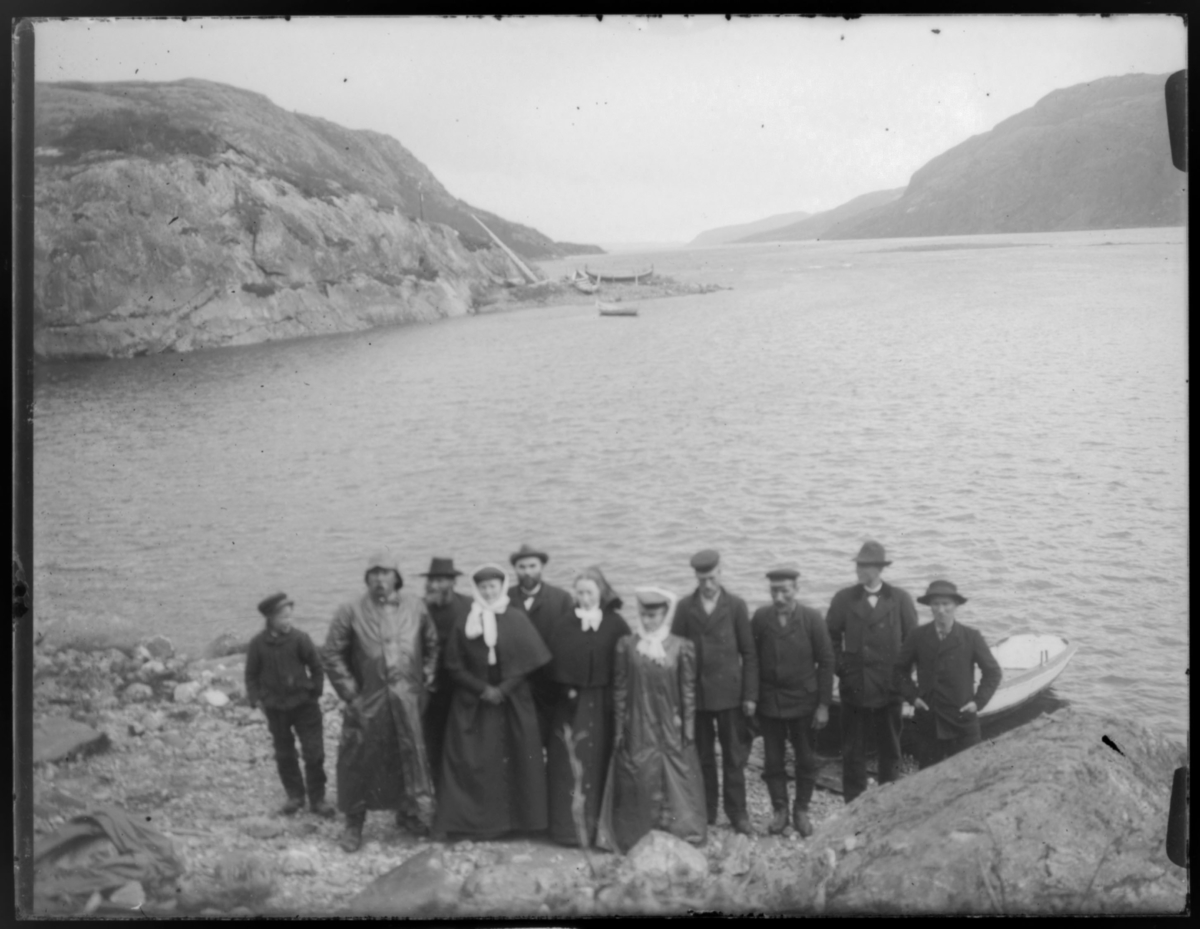 Gruppebilde ved elvebredden av Pasvik elv. I bakgrunnen et ness med båter trekt opp på land og trillebane forbi fossen.