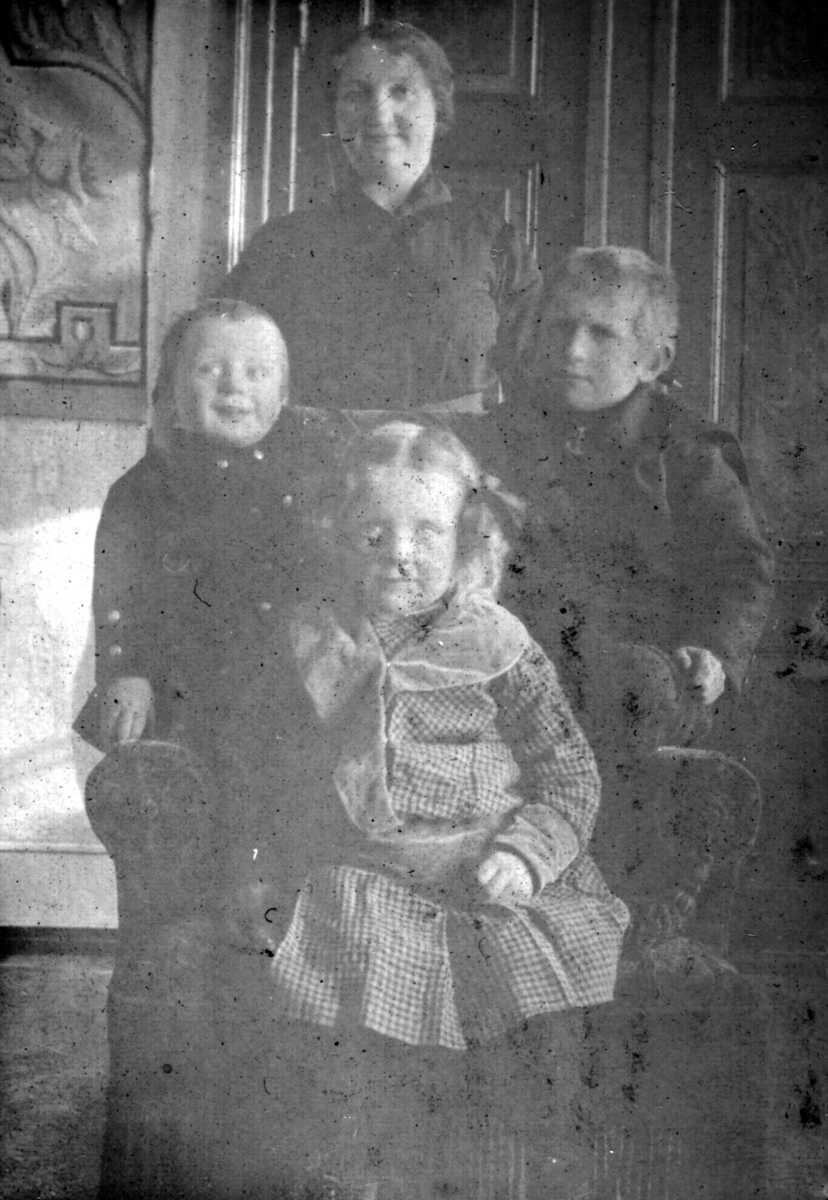 "Hos Soelberg. Loppen." Trolig familien Soelberg som poserer for kameraet. En kvinne står bak en stol. I stolen sitter to gutter og en jente. Jenta er kledd i kjole og har sløyfer i håret.