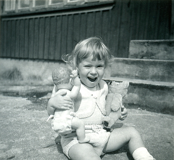Sommaren 1955. Veronika med liten babydocka och nalle som har hållit sig fin. Sparkbyxa och bolero stickad av Birgit i tunt bomullsgarn".