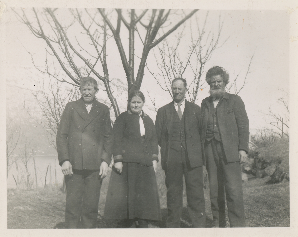 Tre menn og ei kvinne i finere klær poserer for et gruppebilde ute foran et tre.