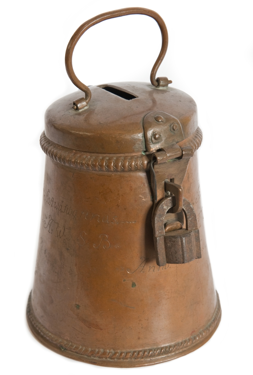 Sparbössa av koppar med hänglås av järn. Inskrift: "Stoftwäfwarnas Fattig Bössa A:W:S:B:I.M.M.D.M.L. Anno 1769."