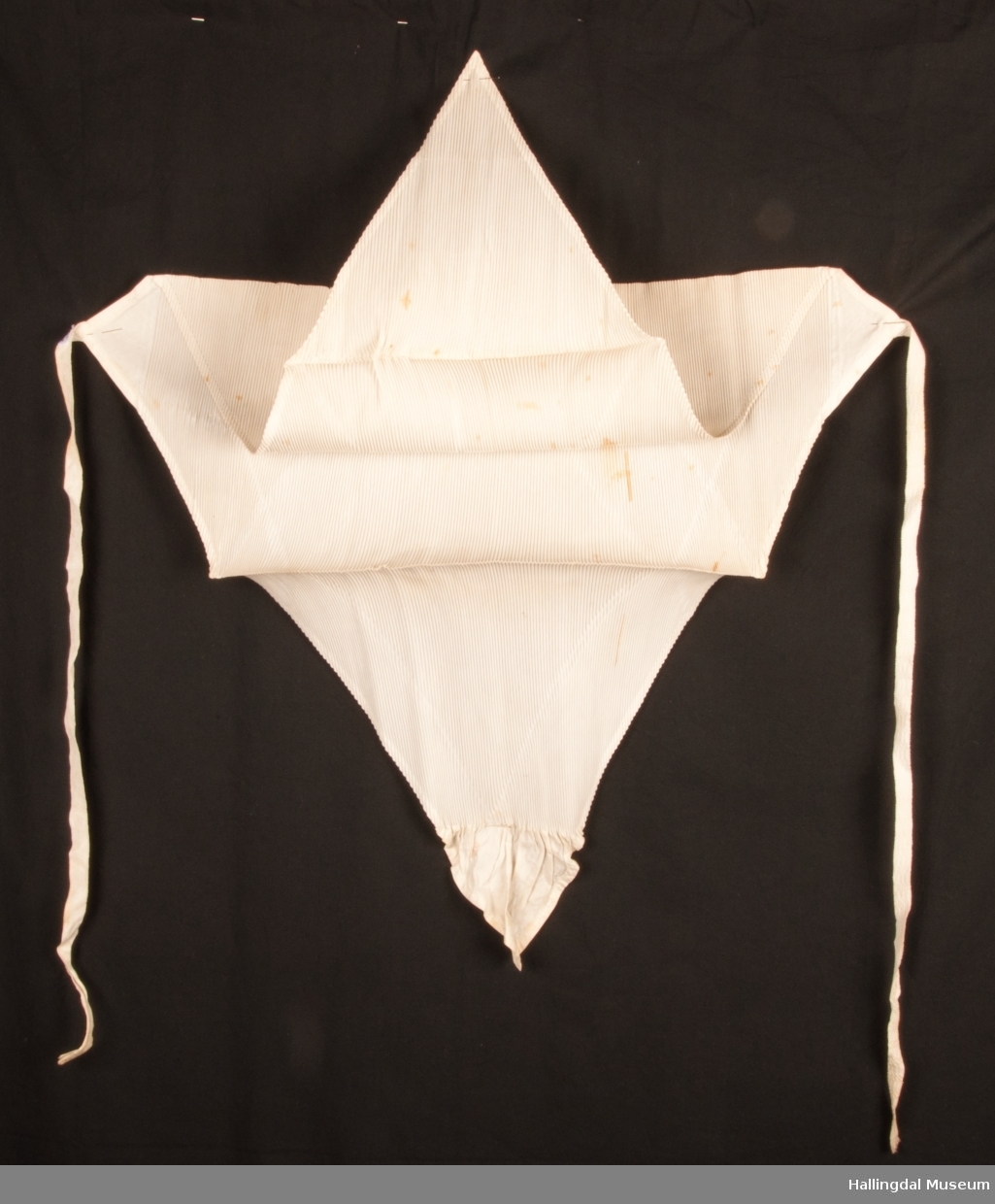 firkantet tøystykke som er brettet 2 ganger (4 flater), stivet og plissert