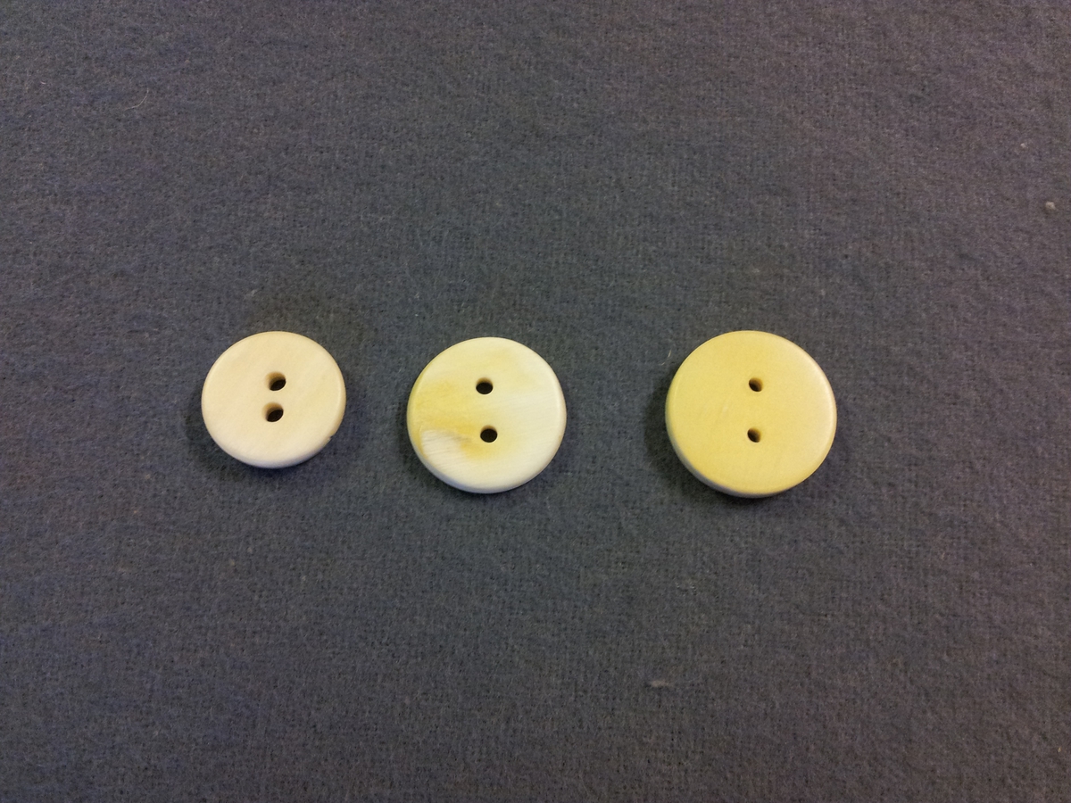 Tre stycken runda, släta hornknappar i något olika storlek med två borrade hål på mitten. Den störsat knappen är något gulare än de två andra som båda har en vitbeige nyans. Diametern går från 16 till 20 mm.