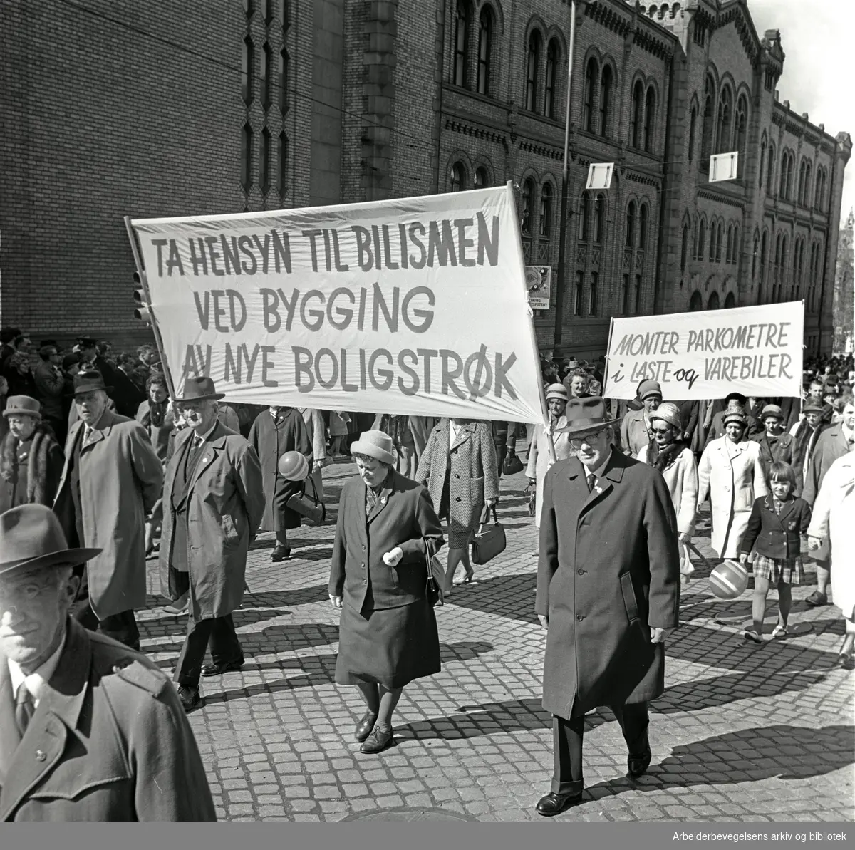 1. mai 1964 i Oslo.Demonstrasjonstoget i Karl Johans gate.Parole: Ta hensyn til bilismen ved bygging av nye boligstrøk.Parole: Monter parkometre i laste og varebiler