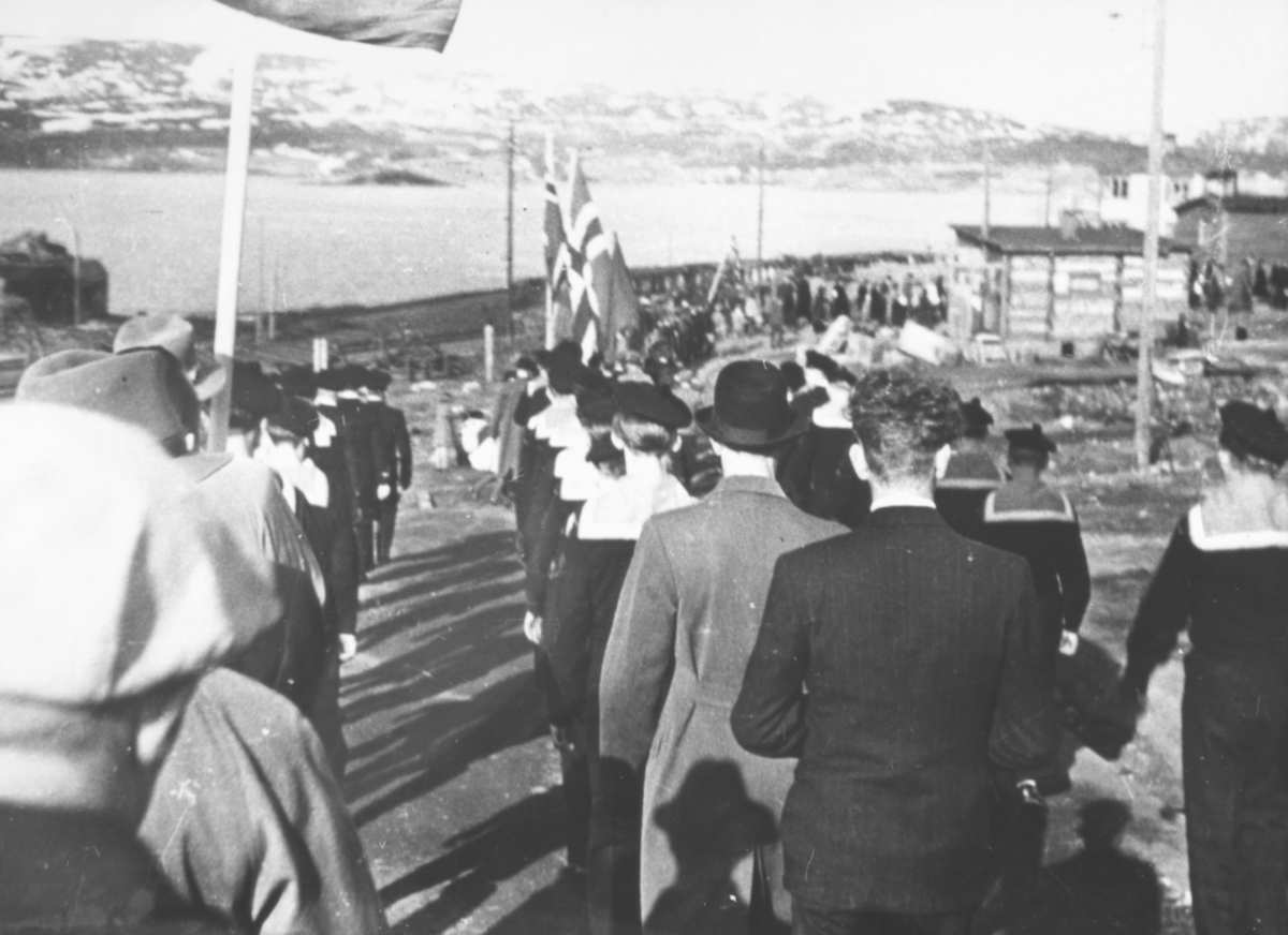 17.Mai i Kirkenes 1945. Toget på vei ned Sjøgaten, fotografert bakfra. Vi ser marinesoldater med uniformer og menn med frakk og hatt.