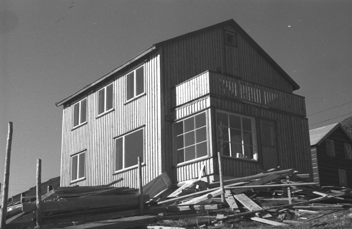 Et gjenreisningshus står ferdig i Honningsvåg med mye material liggende på tomta utenfor.
Arkitekt Ola Hanche-Olsen arbeidet ved Brente Steders Reguleringskontor i 1946. Hovedadministrasjon for gjenreisning av Nord-Troms og Finnmark ble lagt til Harstad og fikk navnet Finnmark kontoret. Landsdelen Nord-Troms og Finnmark blev oppdelt i syv distrikt med hver sin administrasjon. Honningsvåg, distrikt IV, skulle betjene Nordkapp, Lebesby, Porsanger og Karasjok kommune.

Ola Hanche-Olsen har tatt bildene. Han var født 13. mars 1920 i Borre, død 11. februar 1998 i Gjettum. Han var både arkitekt og barnebokforfatter. Han hadde artium fra 1939, arkitekteksamen fra NTH 1946 og arbeidet deretter ved Finnmarkskontoret 1946–48 før han etablerte egen arkitektpraksis. Han debuterte som barnebokforfatter i 1974 med lettlest-boka "Knut og sjørøverne", og skrev i alt 12 bøker. Han var XU-agent 1944-45, og var også en aktiv fjellklatrer og friluftsmann. Ola var gift med Solveig Hanche-Olsen (f. Falkenberg); de fikk 3 barn, blant dem matematikeren Harald Hanche-Olsen.

